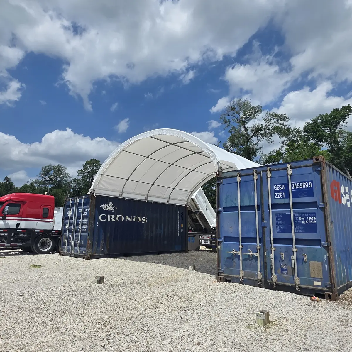 White shipping container canopy shelter covering a truck yard work area between blue containers