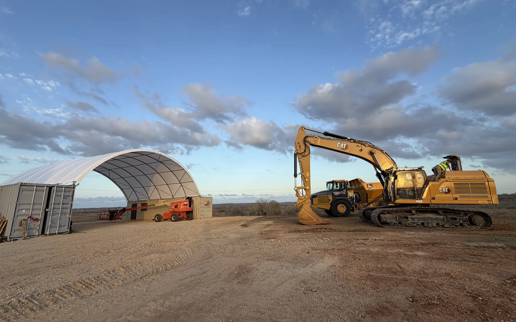 Shipping container canopy beside excavators and heavy construction equipment at an industrial work site