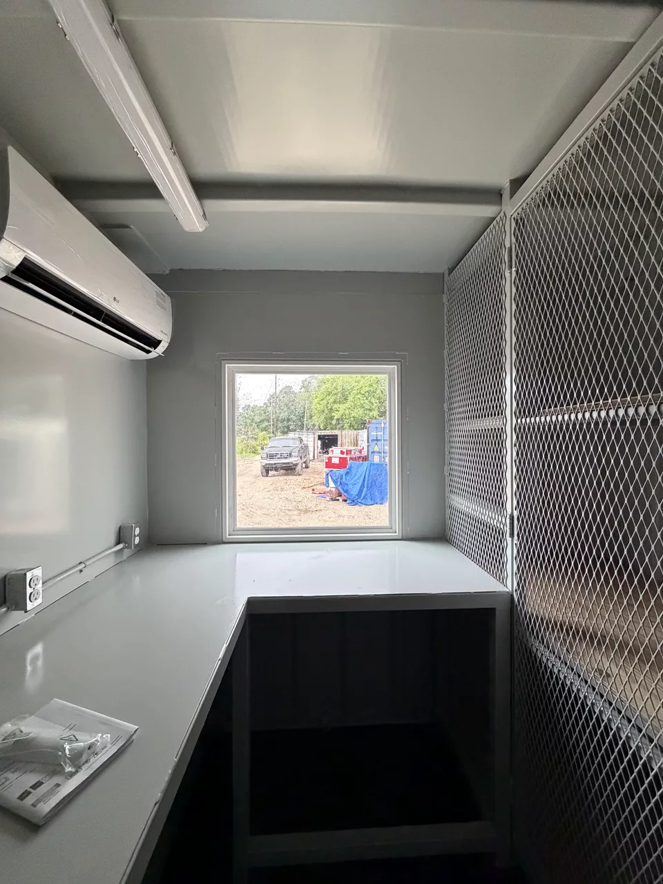 Technical container interior with work counter, mini-split air conditioning, window, and lockable steel mesh equipment partition