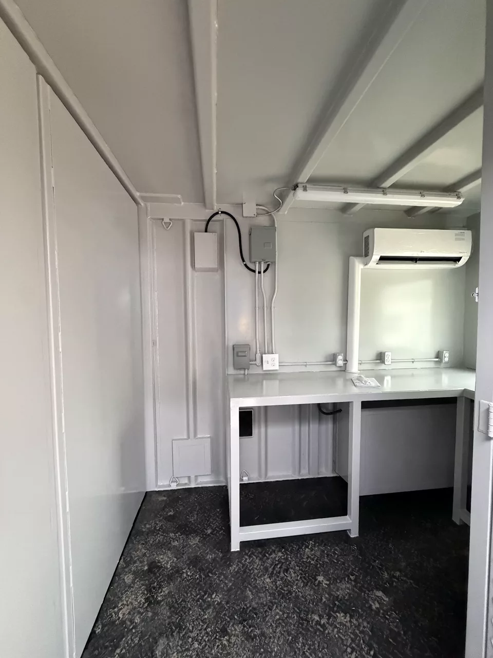 Finished technical container interior with workbench, electrical panels, lighting, outlets, and mini-split air conditioning
